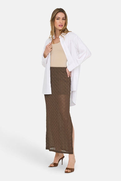Long manteau brun d'ONLY, avec une texture subtile et un haut col, associé à une chemise beige et un blazer blanc.
