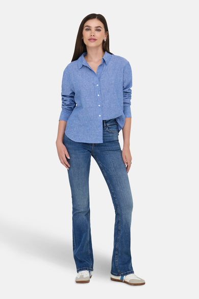 Jean en denim bleu marine à jambes évasées de JDY, portés avec un chemisier rayé bleu et des baskets blanches.