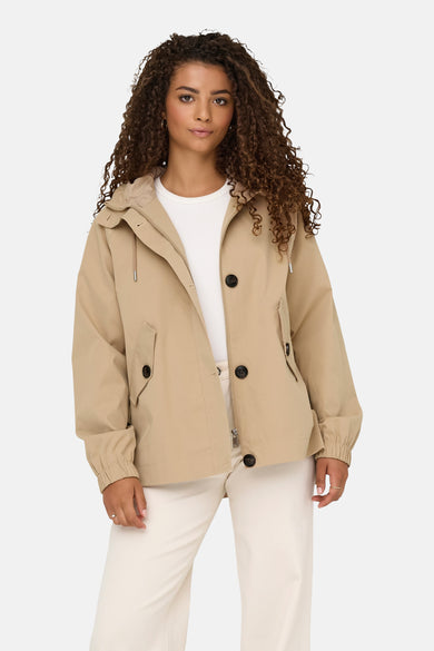 Manteau court beige d'ONLY, avec fermeture à boutons et porté avec un chemisier blanc et des pantalons crème.