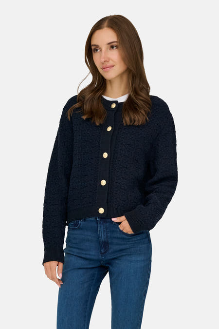 Veste bleue de JDY, avec des boutons dorés et une subtile texture, portée avec un haut blanc et un jean foncé.