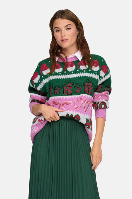 Pull multicolore à col rond de ONLY, avec des motifs de Noël et une jupe plissée verte et des sandales dorées.