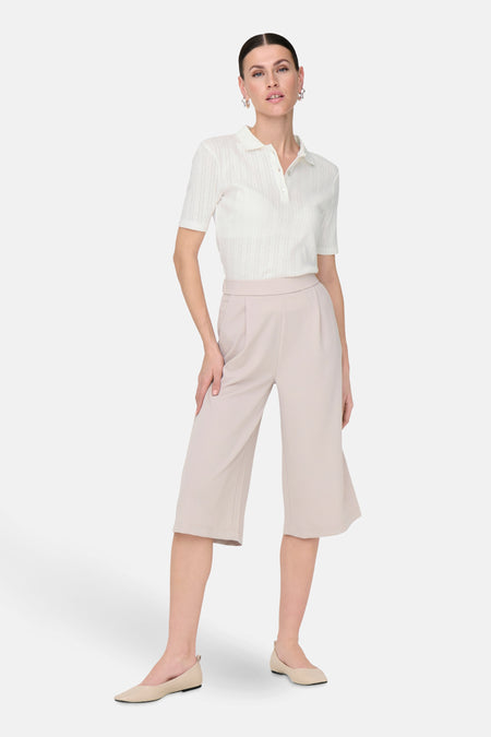 Polo blanc à manches courtes de JDY, avec col boutonné et porté avec une culotte beige et des chaussures plates.