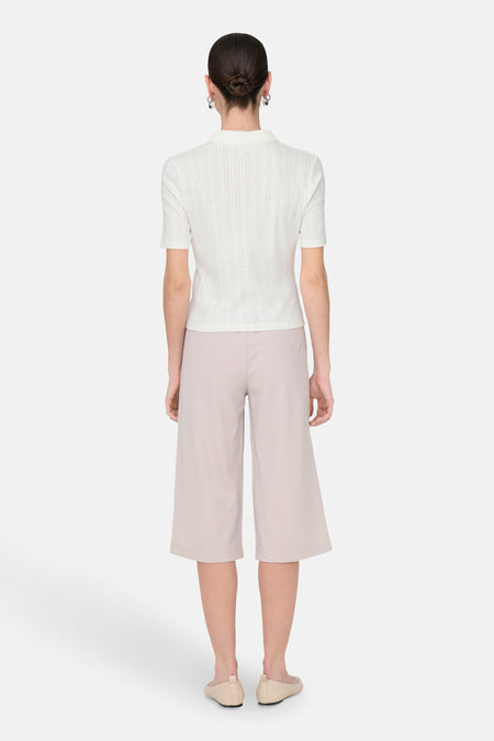 Polo blanc à manches courtes de JDY, avec un subtil motif structuré et associé à des culottes beige et des ballerines.