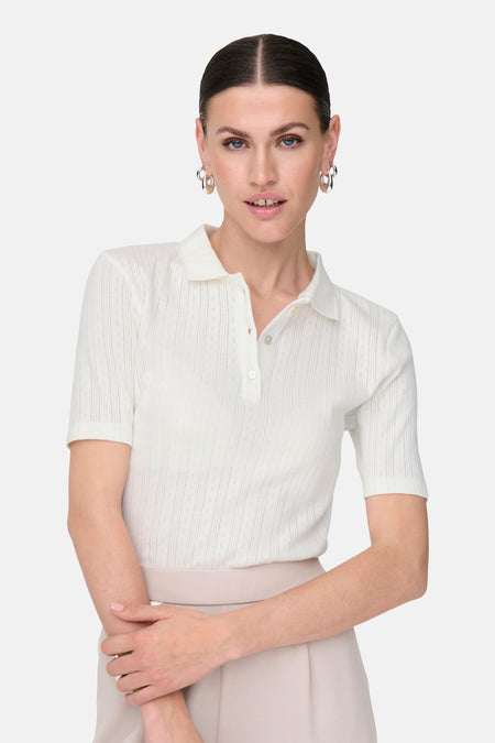 Polo blanc à manches courtes de JDY, avec une fine structure et porté avec des boucles d'oreilles en argent.