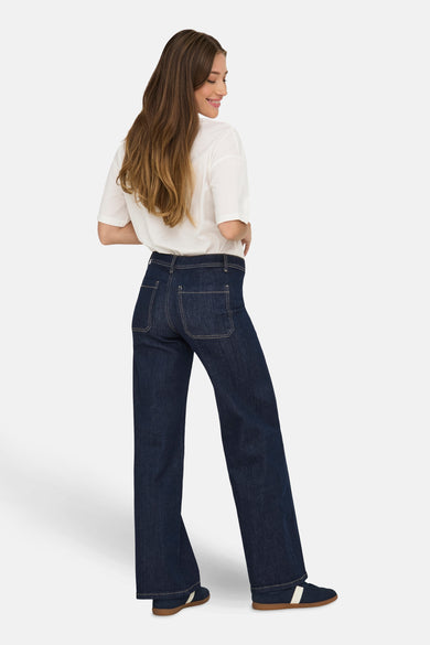 Jean droit en denim bleu marine de JDY, vu de derrière, avec un t-shirt blanc et des baskets bleues.