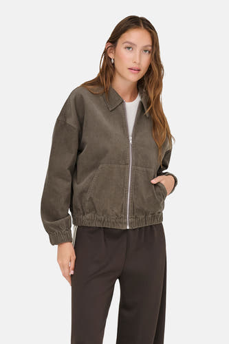 Manteau court brun d'ONLY, avec une fermeture éclair argentée et porté avec un chemisier blanc et un pantalon brun.