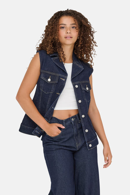 Manteau sans manches en denim bleu marine de ONLY, porté sur une chemise blanche et des jeans coordonnés.