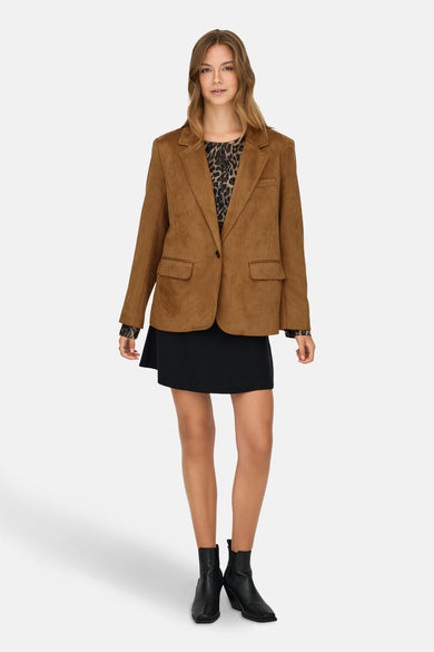 Blazer beige d'ONLY, avec une fermeture à un seul bouton, sur un modèle avec une jupe noire et des bottes.