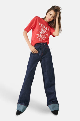 Jean bleu marine large d'ONLY, avec des surpiqures rouges, associé à un T-shirt rouge imprimé.