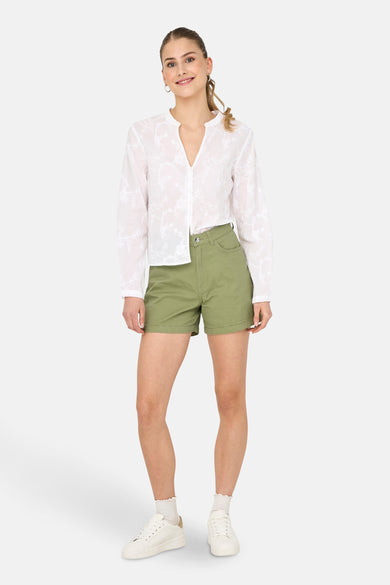 Short vert de ONLY, porté avec une blouse blanche à imprimé et des baskets blanches avec des chaussettes.