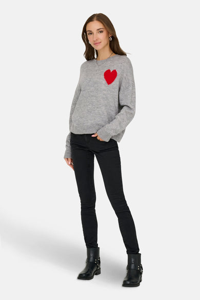 Pull rond gris encolleté JDY, avec cœur rouge sur la poitrine, associé à des jeans noirs et des bottes.