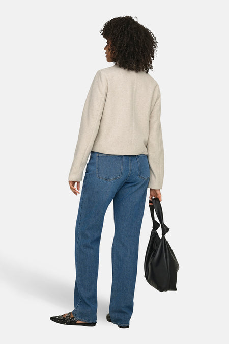 Manteau court écru de ONLY, vu de dos, avec manches longues, combiné avec un jean bleu et un sac à main noir.