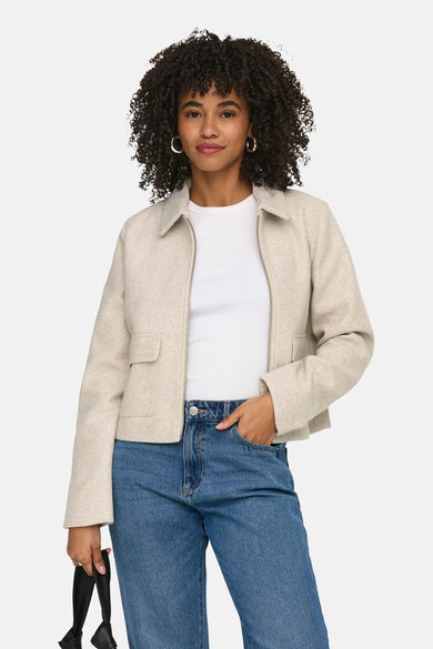 Veste courte écru de ONLY, avec manches longues et poches, combinée avec un jean bleu et un sac noir.