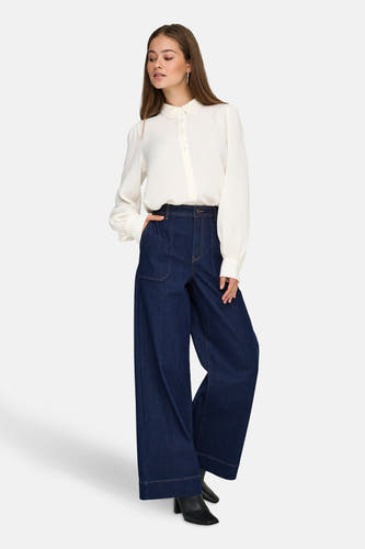 Jeans wide van donkerblauw denim van JDY, met wijde pijpen, op een model met een witte blouse.
