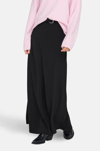 Longue jupe noire de JDY, avec une subtile ceinture et associée à un gilet rose et des bottes noires.