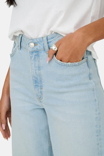 Jean bleu clair large d'ONLY, avec une main dans la poche et une bague en argent.