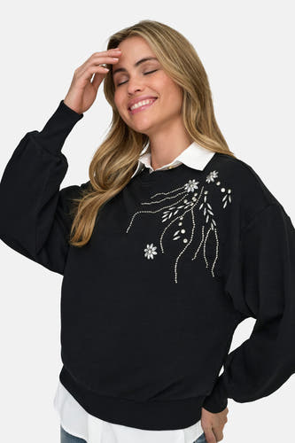 Chemise blanche à manches longues de ONLY®, visible sous une veste noire à fleurs.