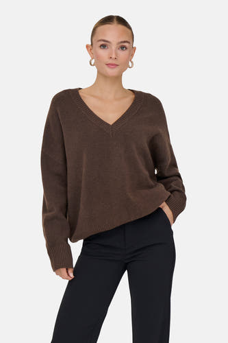 Pull marron avec col en V d'ONLY, porté avec un pantalon noir et des boucles d'oreilles dorées.