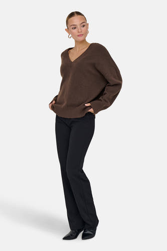 Bruine trui met V-hals van ONLY, gedragen met zwarte broek en gouden oorbellen.
