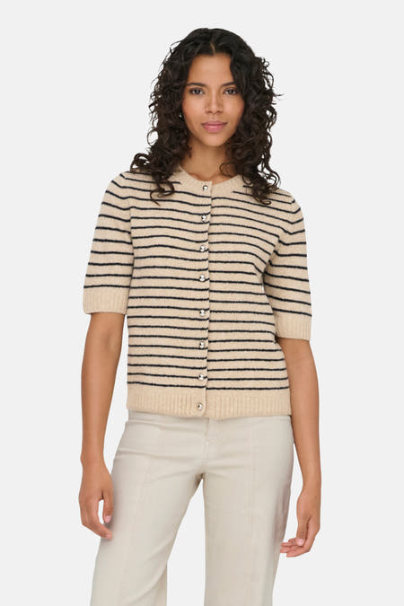 Cardigan écru de ONLY® avec des rayures noires et une rangée de boutons, associé à un pantalon écru et des chaussures noires.