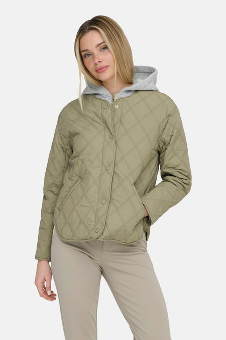 Groene korte jas van ONLY, met een doorgestikt ruitpatroon en knoopsluiting, gecombineerd met een grijze hoodie en beige broek.
