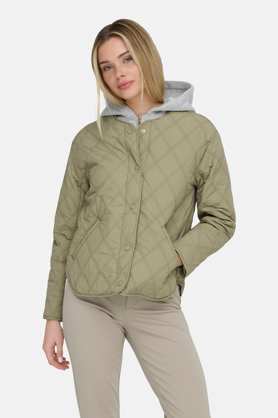Groene korte jas van ONLY, met een doorgestikt ruitpatroon en knoopsluiting, gecombineerd met een grijze hoodie en beige broek.
