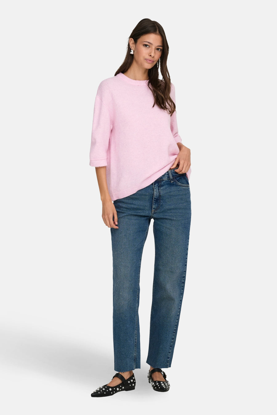 Vrouw met roze trui en blauwe jeans op witte achtergrond.