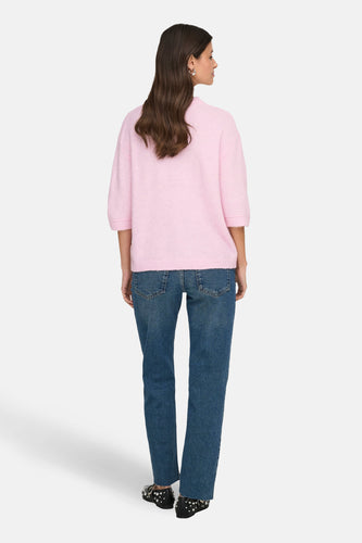 Achterkant van een vrouw met een roze trui en een blauwe spijkerbroek.