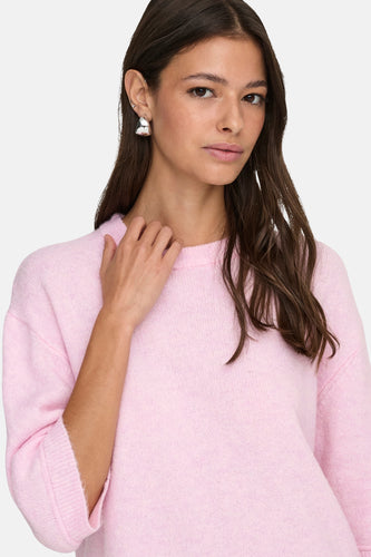 Vrouw in roze trui met zilveren oorbellen.
