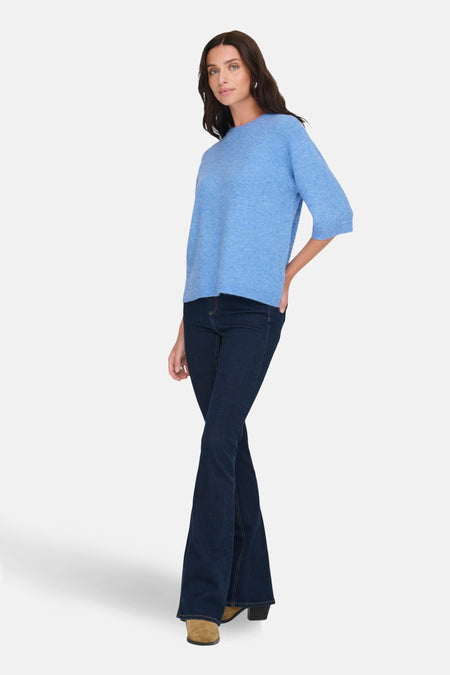 Vrouw met blauwe trui, donkere jeans en bruine schoenen.