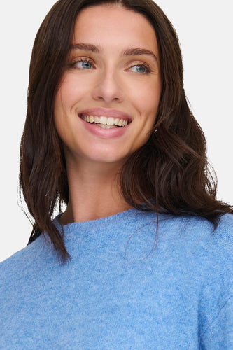 Vrouw in blauwe trui glimlacht.