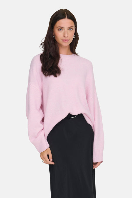 Model draagt een roze sweater en zwarte rok voor een witte achtergrond.