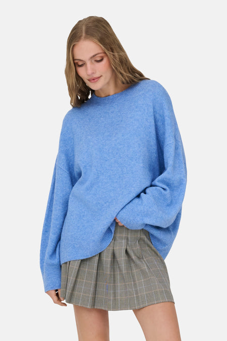 Vrouw met een blauwe oversized trui en geruite rok.

