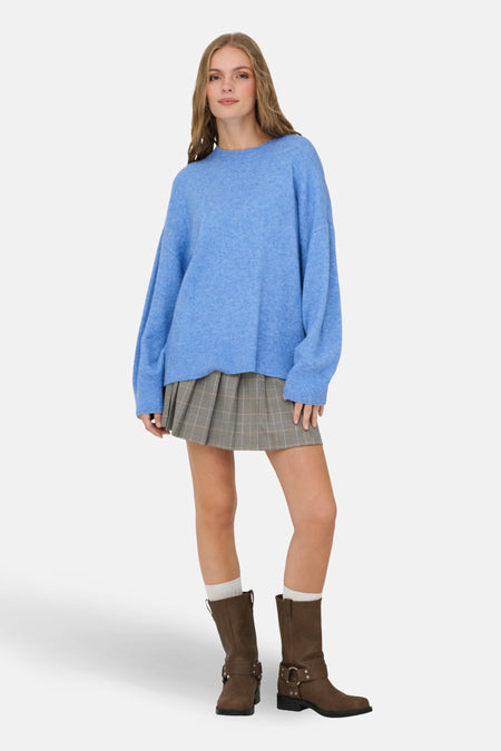 Vrouw, blauwe trui, geruite rok, bruine laarzen.