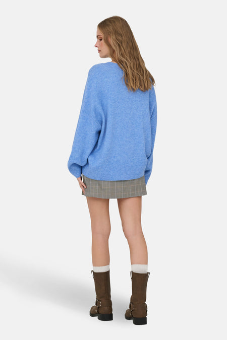 Vrouw, rug, blauwe trui, geruite rok, bruine laarzen, witte sokken.