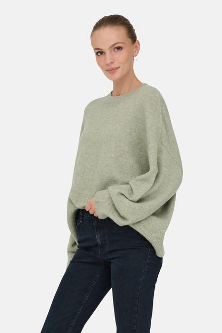 Vrouw in groene trui en donkere jeans.
