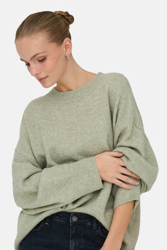 Vrouw in groene oversized trui en donkere jeans.