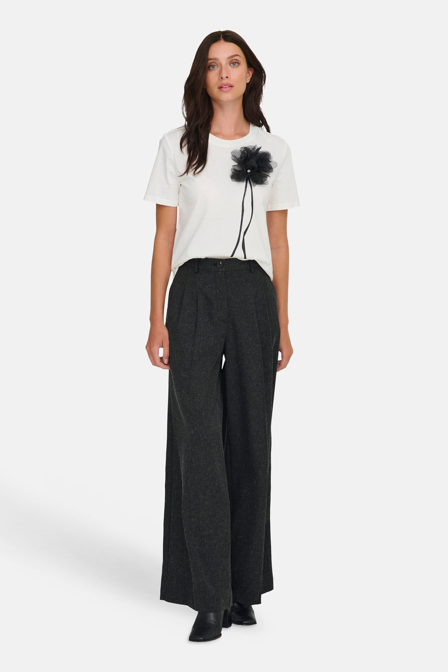 Vrouw in witte T-shirt met zwarte bloem en wijde, grijze broek.