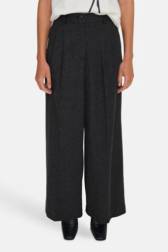 Een vrouw in een witte top en een wijde, donkergrijze pantalon.