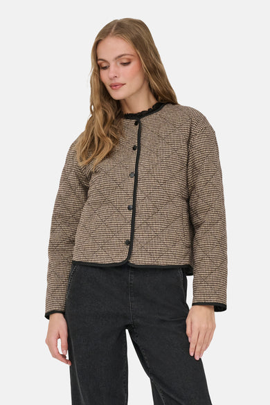 Manteau court brun de JDY, avec un motif à carreaux et des manches longues, porté avec un pantalon noir et des bottes brunes.