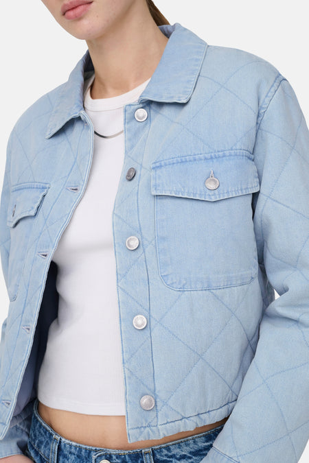 Veste en jean bleu clair ONLY, avec fermeture à boutons, poches poitrine et motif matelassé à carreaux, portée sur un débardeur blanc et un jean.