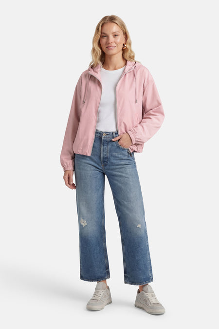 Manteau rose de ONLY®, avec capuche, longues manches, fermeture éclair et porté avec un t-shirt blanc et des jeans bleus.