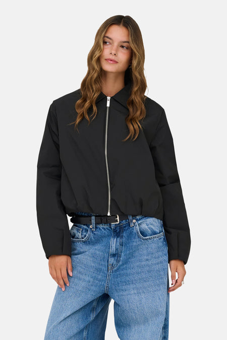 Zwarte korte jas van ONLY, met een zilverkleurige rits en gedragen met een blauwe jeans en zwarte riem.
