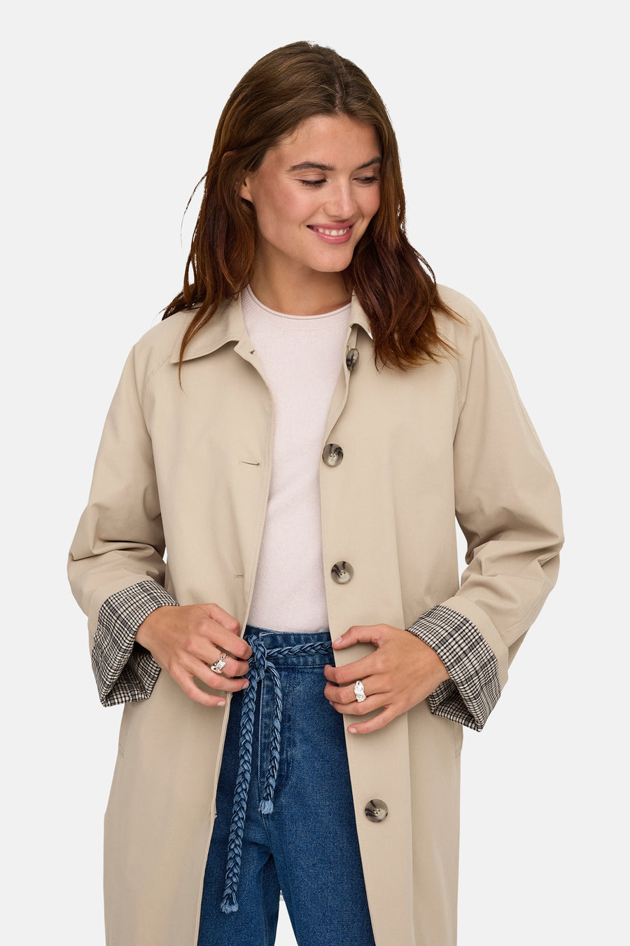 Beige lange jas van ONLY®, met een geruite omslag en geknoopte blauwe jeans.
