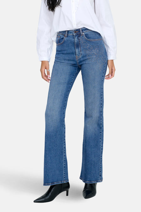 Jeanon denim bleu marine à jambes évasées ONLY avec des détails brodés sur les poches, associé à une chemise blanche.