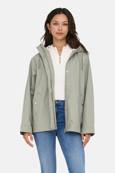 Kaki de pluie ONLY, avec un capuchon, portés avec une chemise blanche et des jeans bleus.