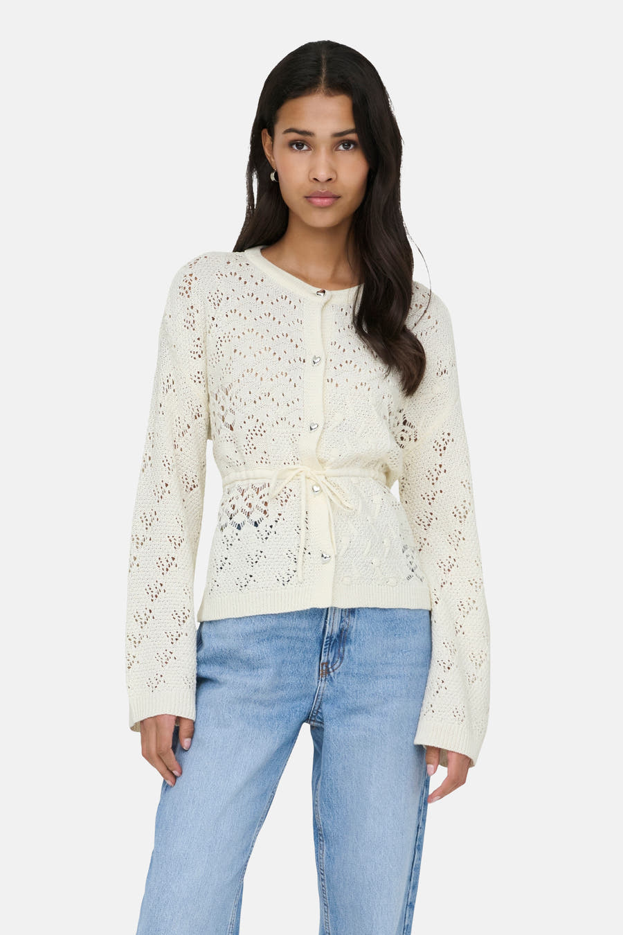 Gilet écru de ONLY, avec une texture ajourée et un col en tricot, associé à des jeans bleus et des chaussures noires.