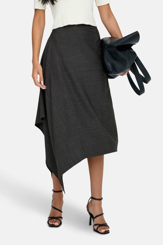 Vrouw met gestreepte rok, witte top en zwarte hakken, met een zwarte tas in de hand.