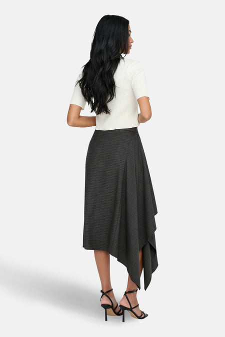 Vrouw in witte top en asymmetrische, gestreepte rok met zwarte hakken.