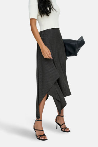 Model met een witte top, grijze rok met krijtstreep en zwarte sandalen met hak.